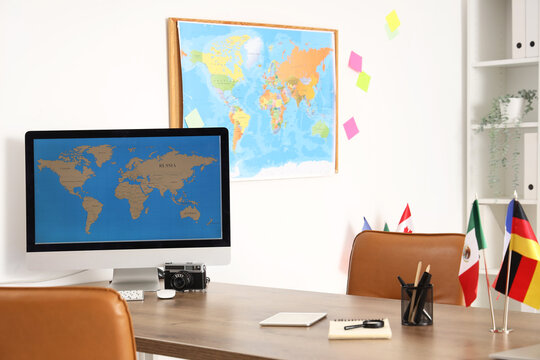 Computer monitor with world map and different flags on table in travel agency