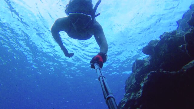 selfie of an young female woman asian free diver wearing bikini snorkel mask holding gopro camera swim descent down into water swimming along at the bottom around coral reef through narrow passages th