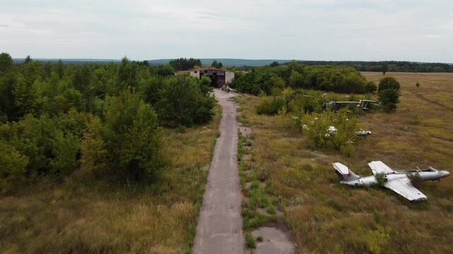 Aerial view of abandoned airbase field with retired airplanes and weathered hangar surrounded by natural greenery
