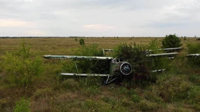 Drone shot of weathered An-2 Antonov biplane abandoned in old airfield, aviation remains in greenery