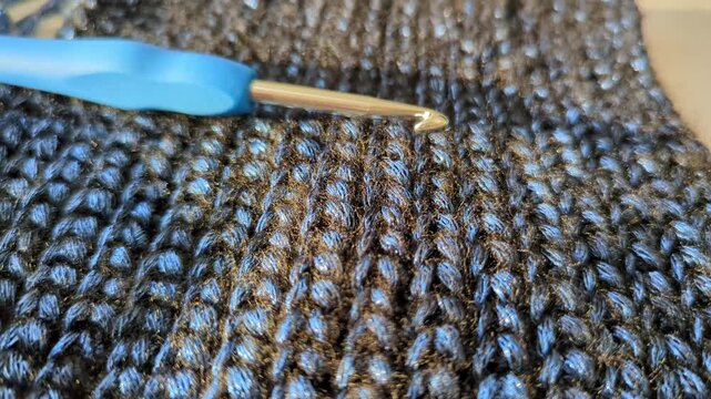 Crochet hook on handmade warm textured, shiny dark blue fabric. Detailed stitches textile craft work