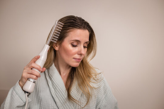 Woman uses darsonval for massage head's skin. Receiving electric darsonval facial massage procedure. 