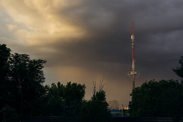 Obraz premium Tall telecommunication tower against dramatic stormy sky at sunset, urban infrastructure concept.