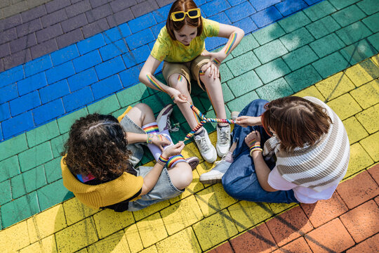 People sitting on rainbow pavement holding colorful string