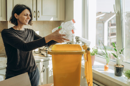 Smiling person sorting plastic bottles into yellow recycling bin