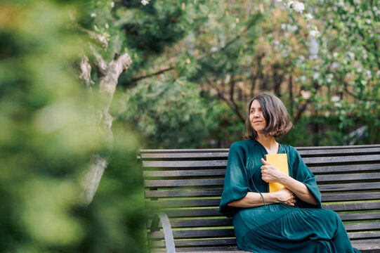Woman sitting on a park bench reading a book in a spring garden