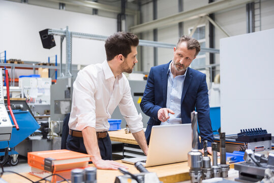 Two men at table in factory shop floor with laptop