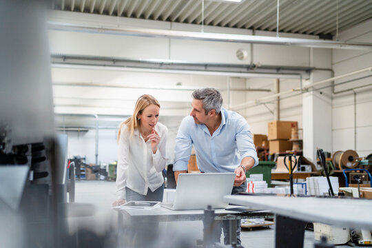 Businessman looking at colleague discussing ideas at desk in factory