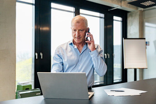 Manager on cell phone using laptop in modern office
