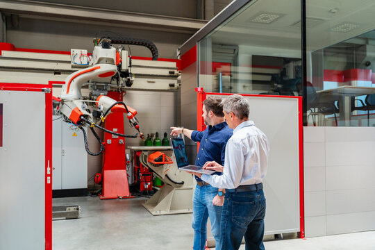 Engineers programming industrial robot with laptop in factory