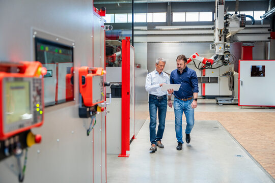 Manager and engineer walking with tablet in modern factory indoors