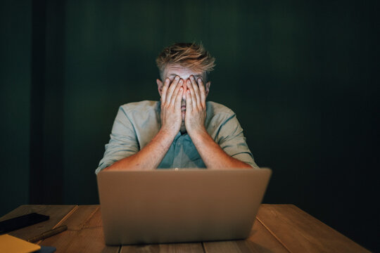 Tired man sitting in office, working late in his start-up company, covering eyes