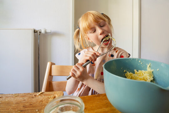 Girl tasting cake batter from wire whisk at home