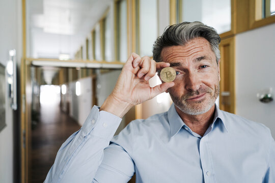 Businessman covering eyes with bitcoin while standing at office