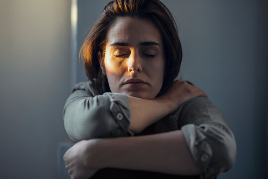 Woman with eyes closed sitting in dark at home