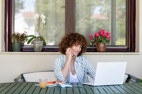Smiling freelancer working from home outdoors with laptop and phone