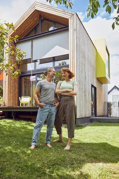 Mature man with hands in pockets looking at woman while standing outside tiny house