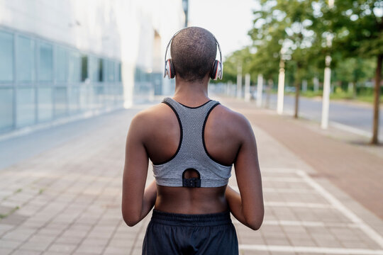 Young woman with shaved head listening music through headphones while standing on footpath
