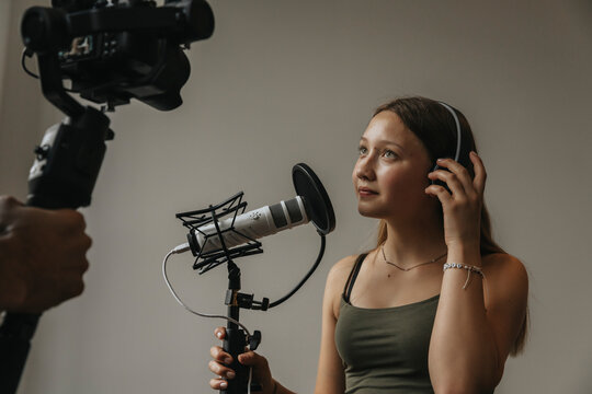 Teenage girl looking at camera while singing over microphone against wall in studio