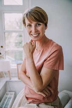 Smiling woman with hand on chin sitting at home