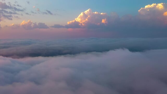 Stunning aerial view of fluffy clouds drifting across sunset sky above thick fog layer covering horizon in peaceful atmosphere.
