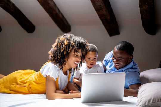 Smiling family using laptop with son while lying on bed at home