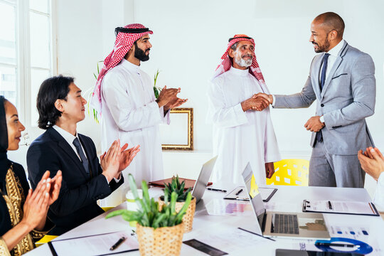 Diverse corporate team clapping during handshake in Riyadh office