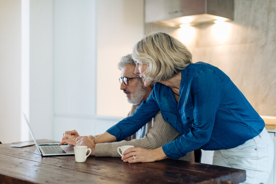 Mature man with wife using laptop on kitchen table at home