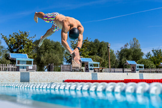 Athlete diving into an outdoor swimming pool from a starting block
