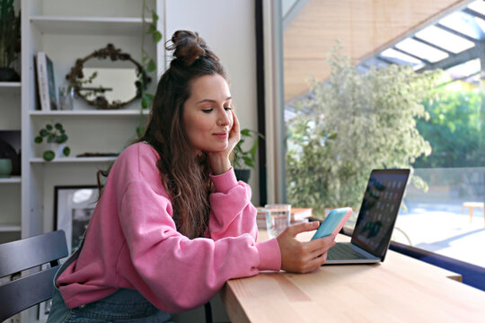 Businesswoman with hand on chin using smart phone at coffee shop