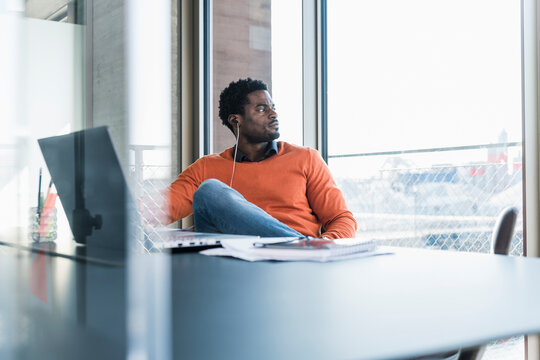 Casual businessman with earphones sitting at desk looking out of window