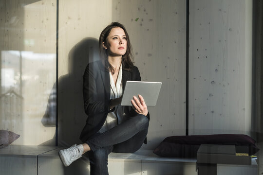 Businesswoman with tablet sitting in lounge area in office