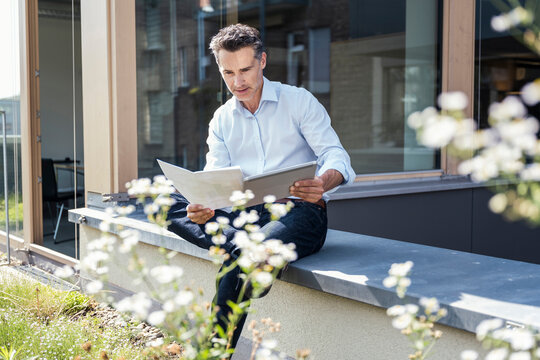 Businessman analyzing document while using digital tablet