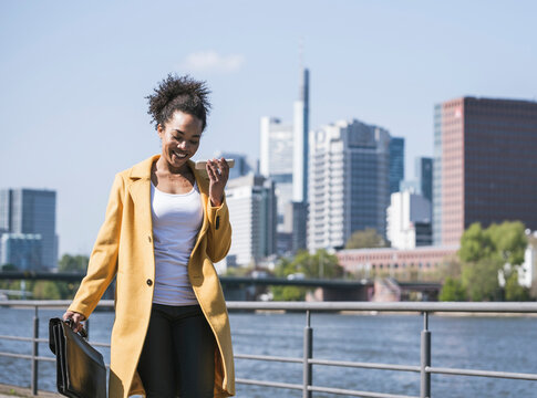 Smiling businesswoman sending voicemail through mobile phone on sunny day
