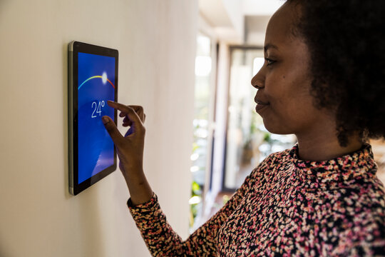 Woman adjusting smart home thermostat temperature on wall indoors