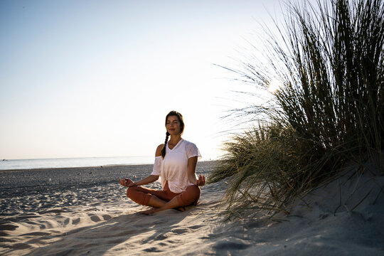 Woman practicing yoga and meditating on a sandy summer beach