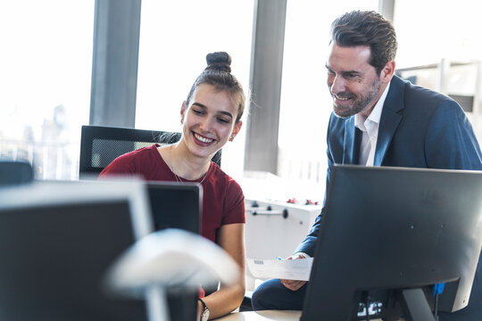 Smiling executive and employee collaborating at office desk