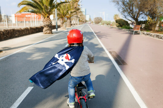 Spain, Barcelona, back view of little boy with a pirate cape riding bicycle on an empty street