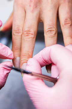 Professional manicurist wearing gloves removing cuticle from a client's hand