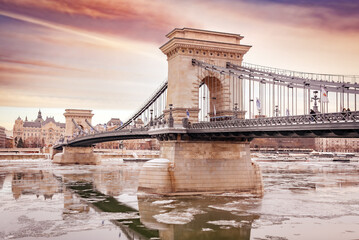 Naklejka premium Szechenyi Chain Bridge over the frozen Danube river at dramatic sunset, Budapest, Hungary
