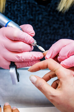 Manicurist hand in pink gloves using electric nail file on client's nail in salon