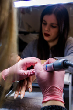 Manicurist wearing pink gloves doing a nail care treatment on client hands with a drill