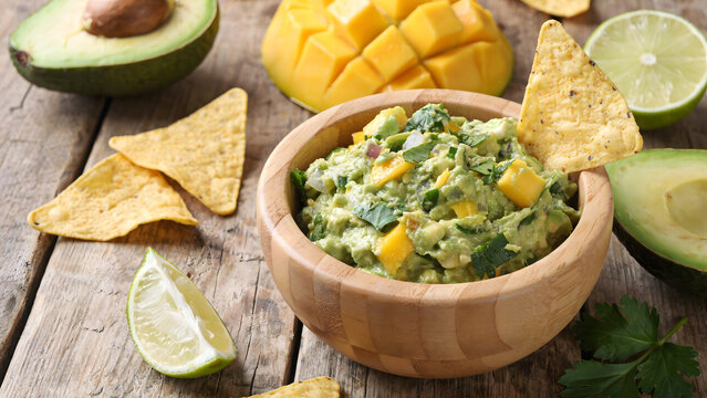 Fresh homemade guacamole served in a wooden bowl with mango and tortilla chips