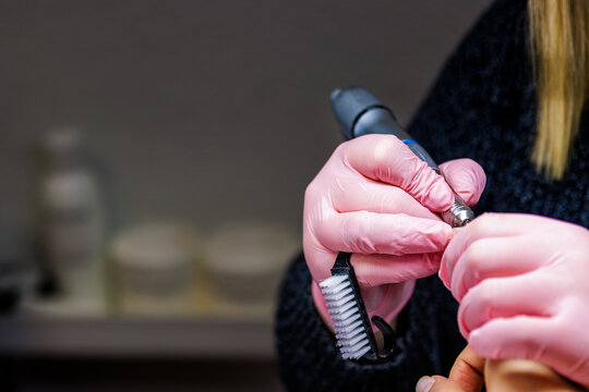 Manicurist wearing pink gloves performing professional nail care with a drill tool