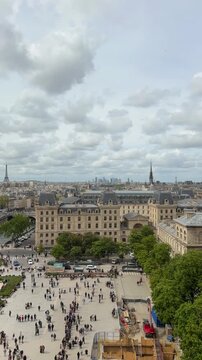 TIMELAPSE | Aerial view of a crowd of tourists waiting in line in the parvis of Notre Dame Cathedral, with the Parisian skyline, the Eiffel Tower, and the business district of La D&eacute;fense