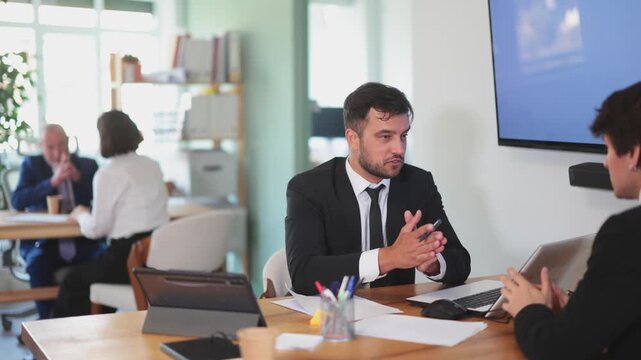 Professional adult male lawyer or bank employee talking and signing loan agreement with young guy client in modern bank office