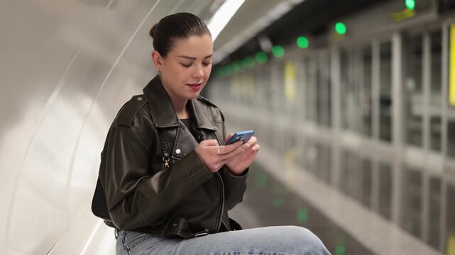 Young woman waiting for train at subway station with mobile phone
