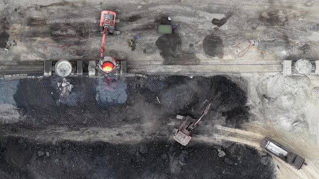 Heavy machinery and excavators process molten slag at a large industrial steel factory site in Hungary during daytime operations.