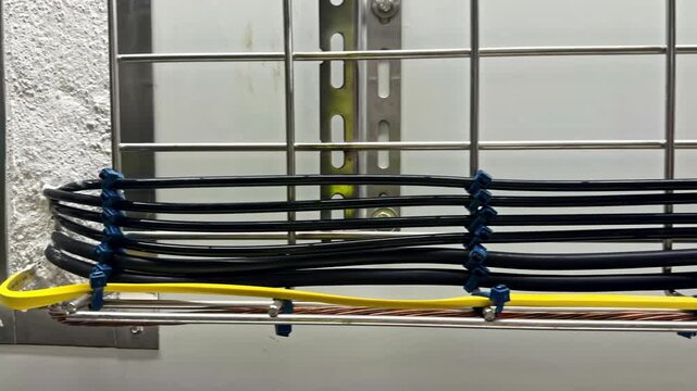 A structured arrangement of black and yellow cables is neatly secured on a metal rack within an industrial setting.