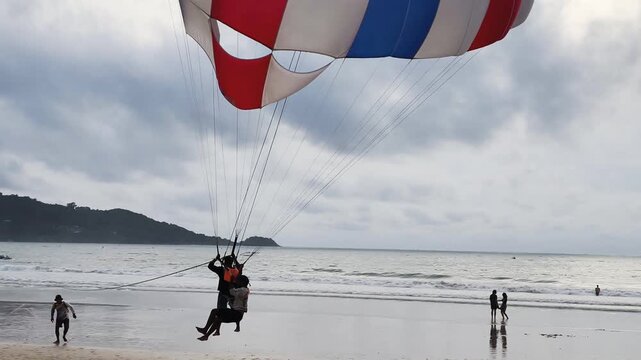 Exciting parasailing landing moment shows professional instructor smoothly touching sandy beach. This successful parasailing landing moment guarantees safe finish for tourists at seaside resort.